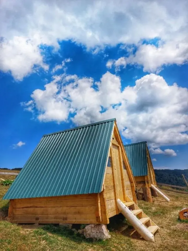 Small A-frame cottage with a green roof under white clouds